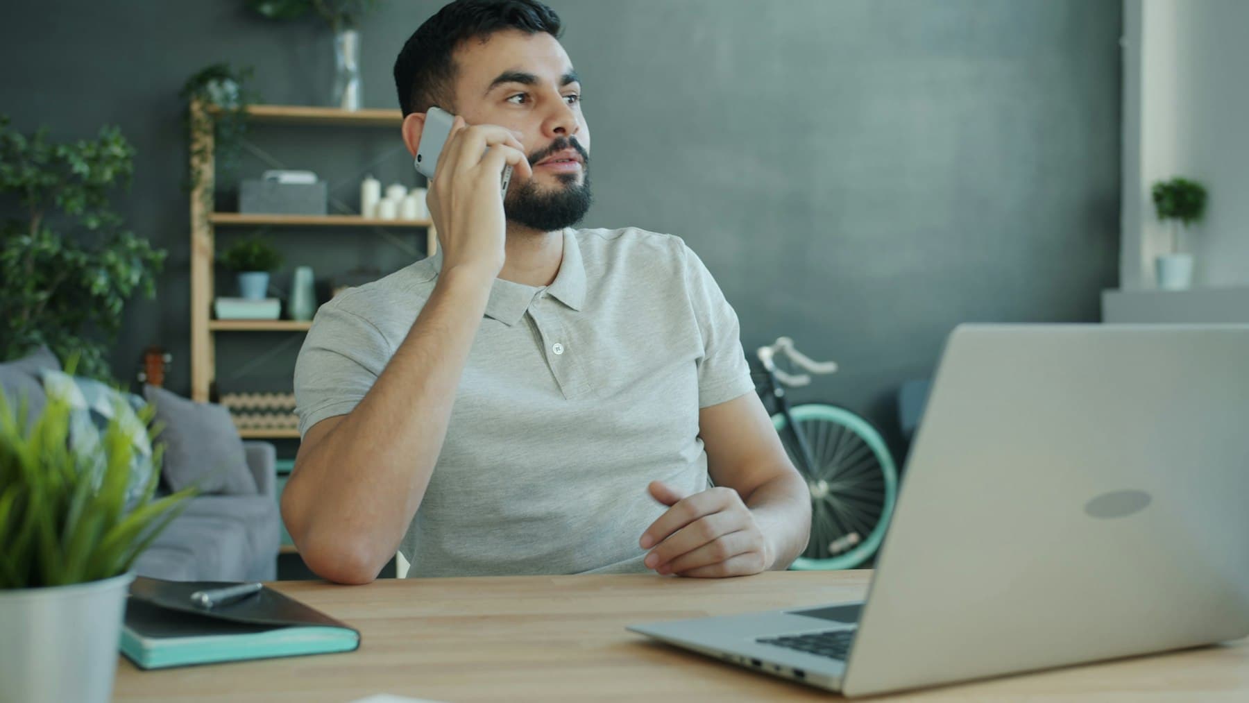 Man i telefonsamtal vid sitt skrivbord med laptop framför sig